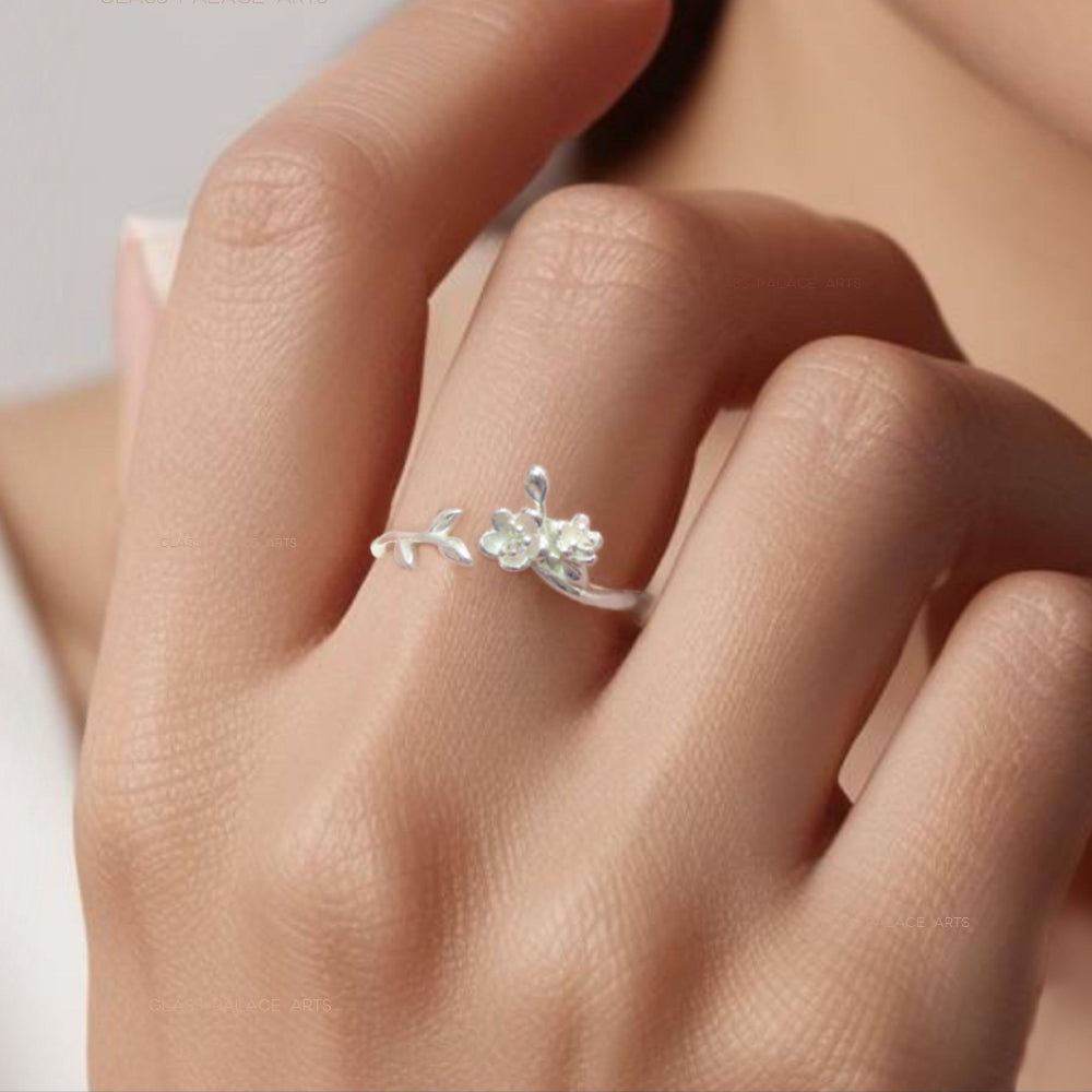 A silver floral ring with an adjustable band featuring a blooming rose design, worn on a person's finger.