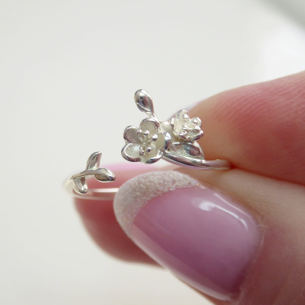 A silver floral ring with an adjustable band featuring a blooming rose design, worn on a person's finger.