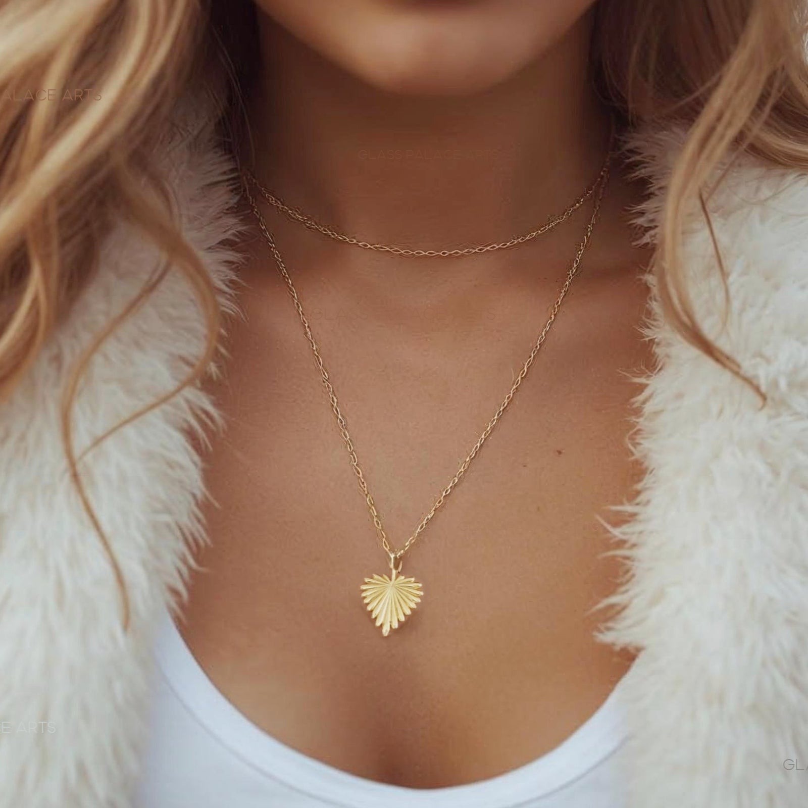 Woman wearing a gold necklace with a heart pendant, dressed in a white fur coat and white top.