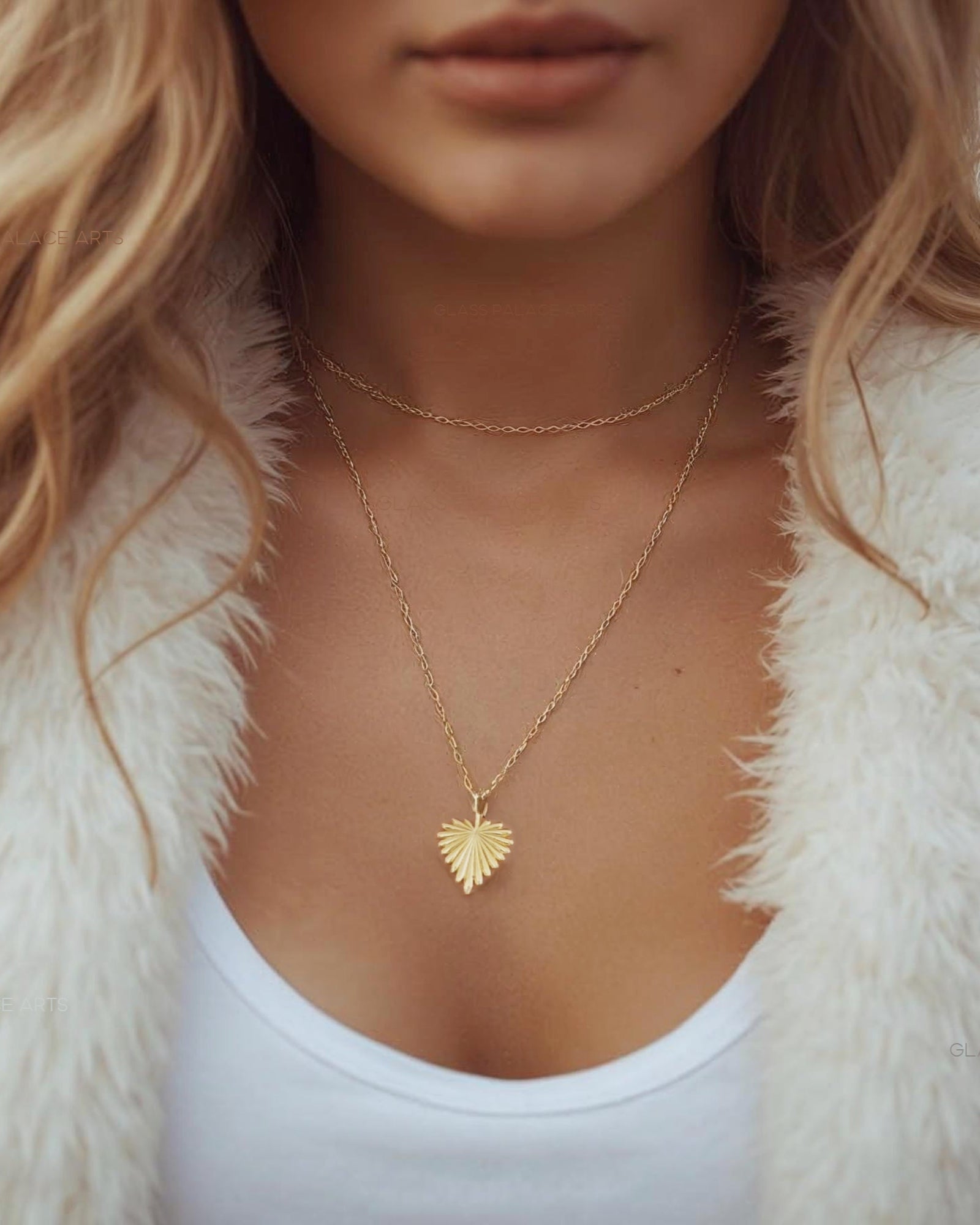 Woman wearing a gold necklace with a heart pendant, dressed in a white fur coat and white top.