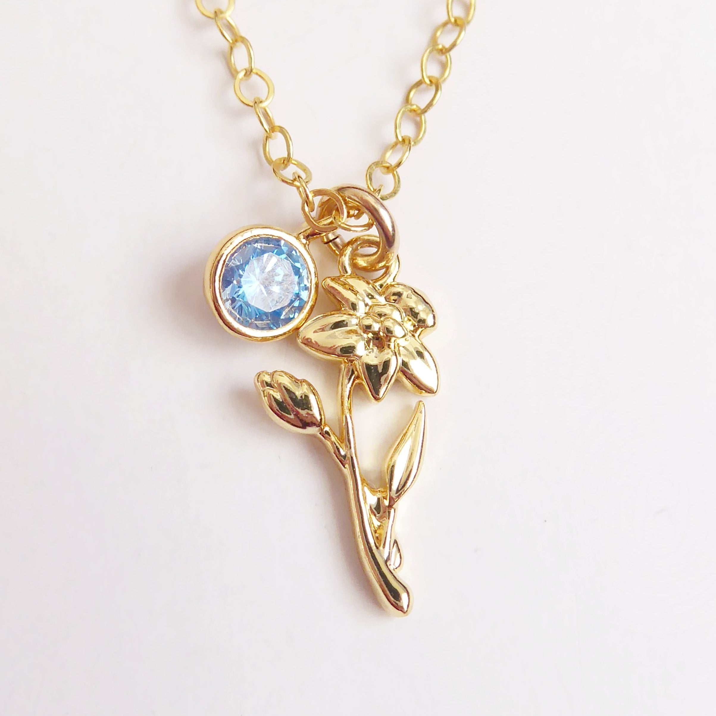 Gold necklace with a blue gemstone and floral design on a white background