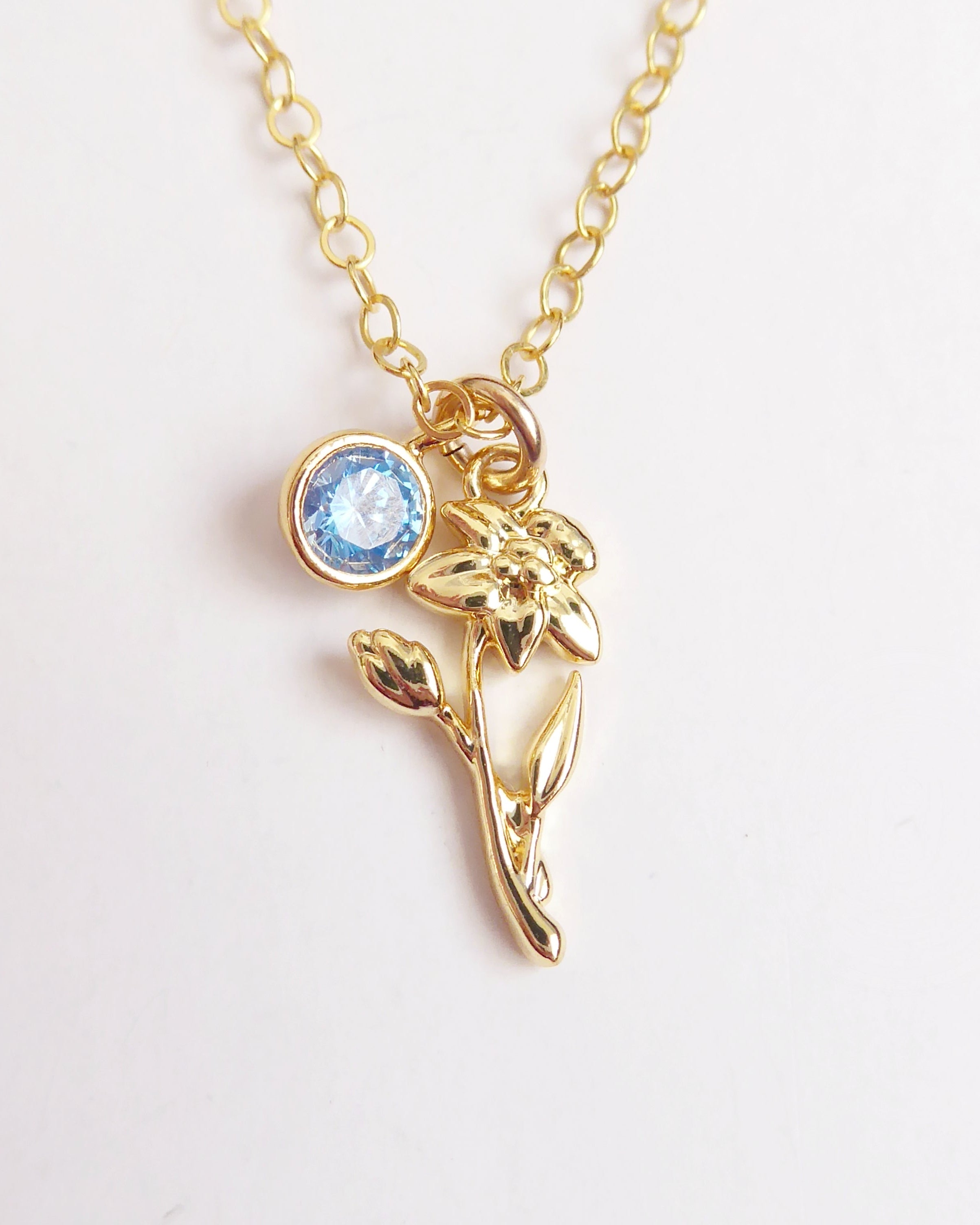 Gold necklace with a blue gemstone and floral design on a white background