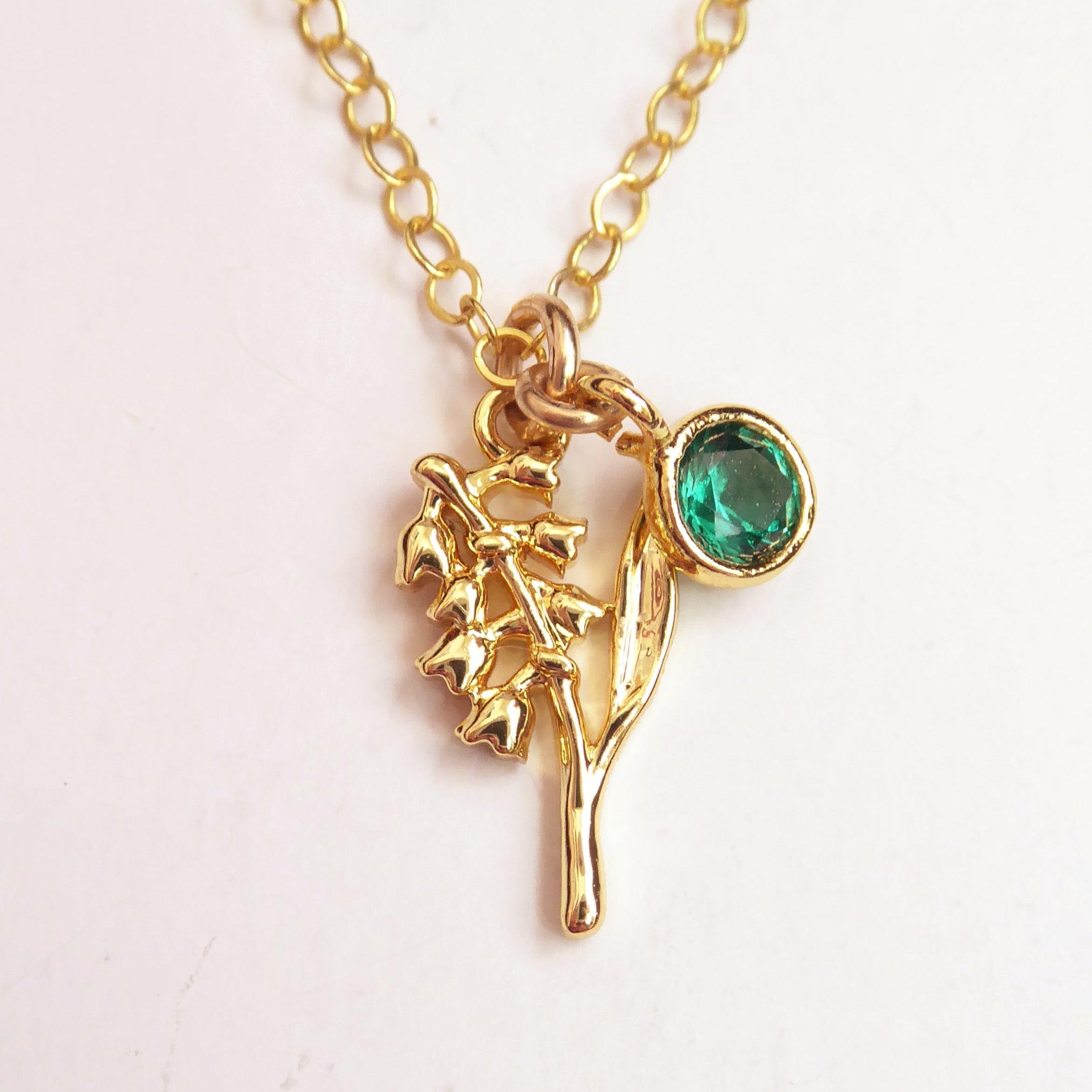 Gold necklace with a green gemstone pendant on a white background
