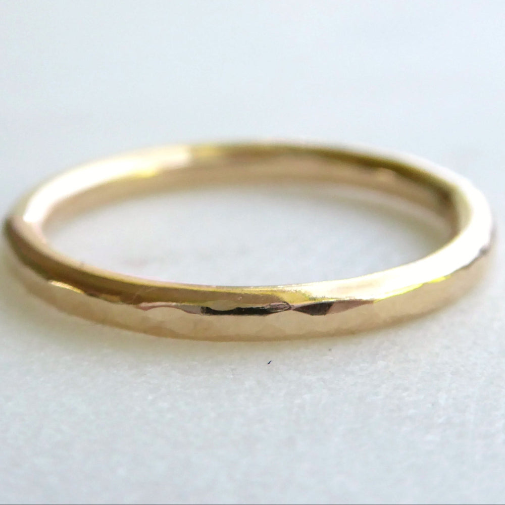 A shiny, gold-colored, hammered texture ring on a white background.