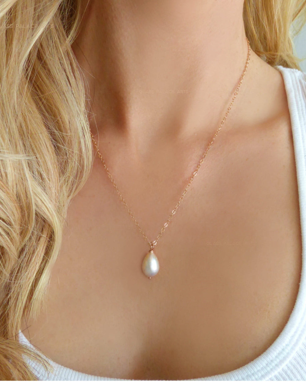 A woman wearing a white top modeling a teardrop-shaped freshwater pearl necklace in rose gold.