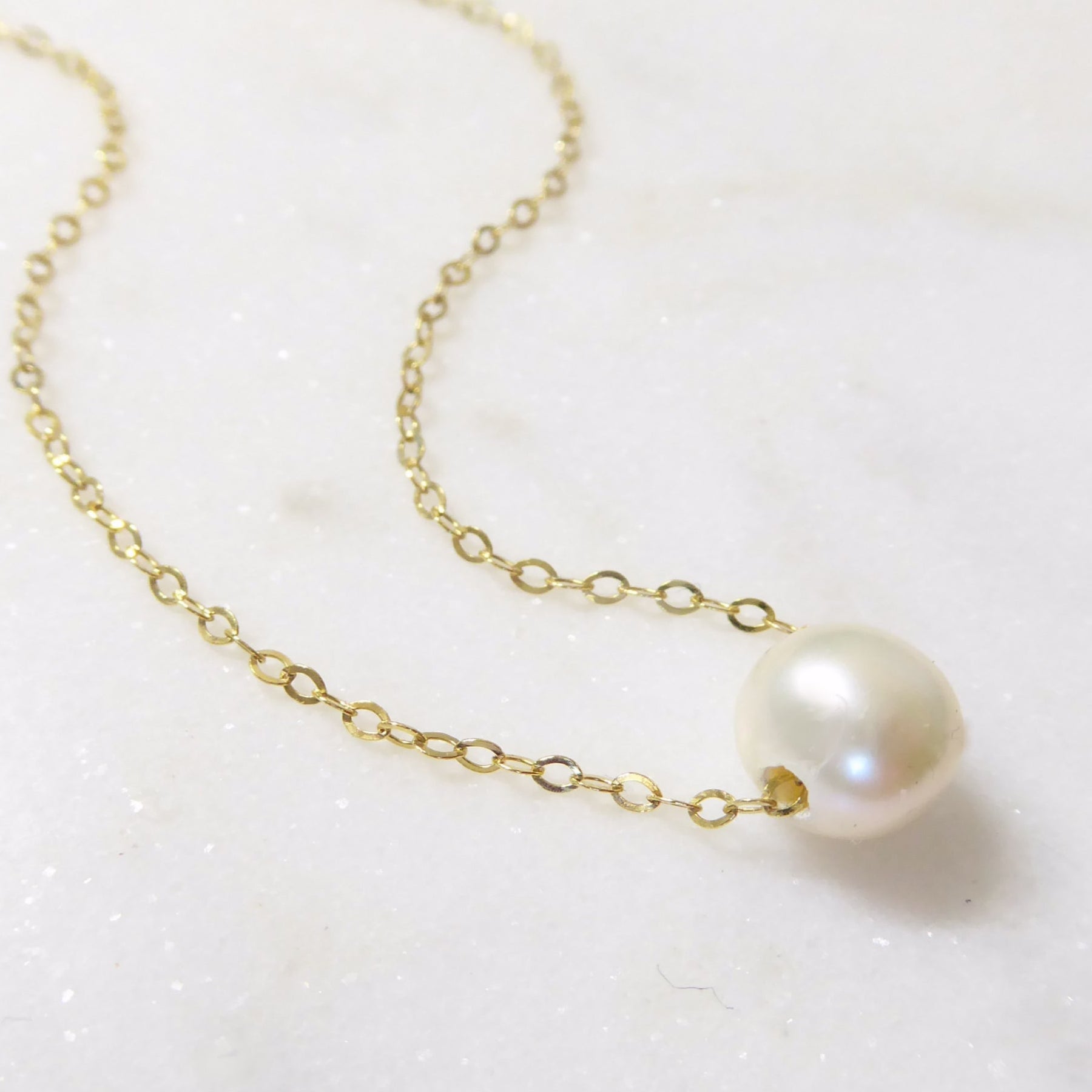 Gold chain necklace with a single pearl on a white background