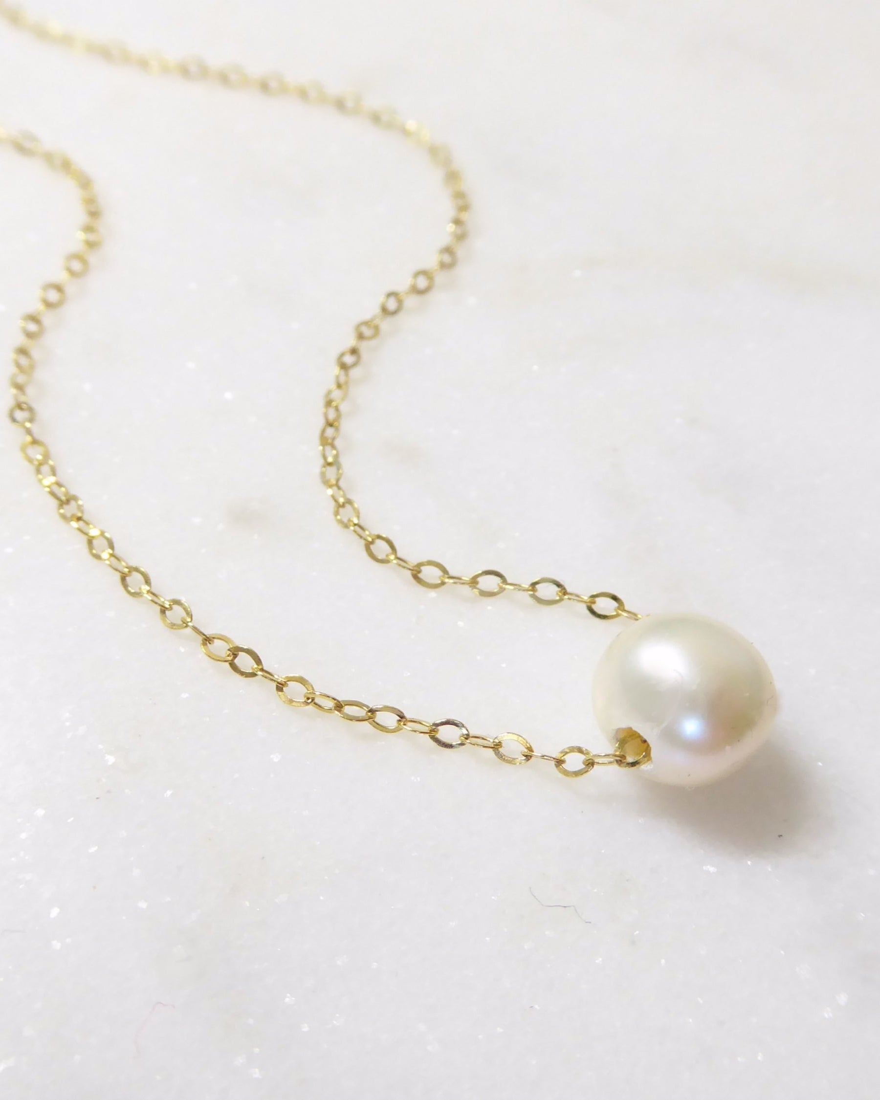 Gold chain necklace with a single pearl on a white background