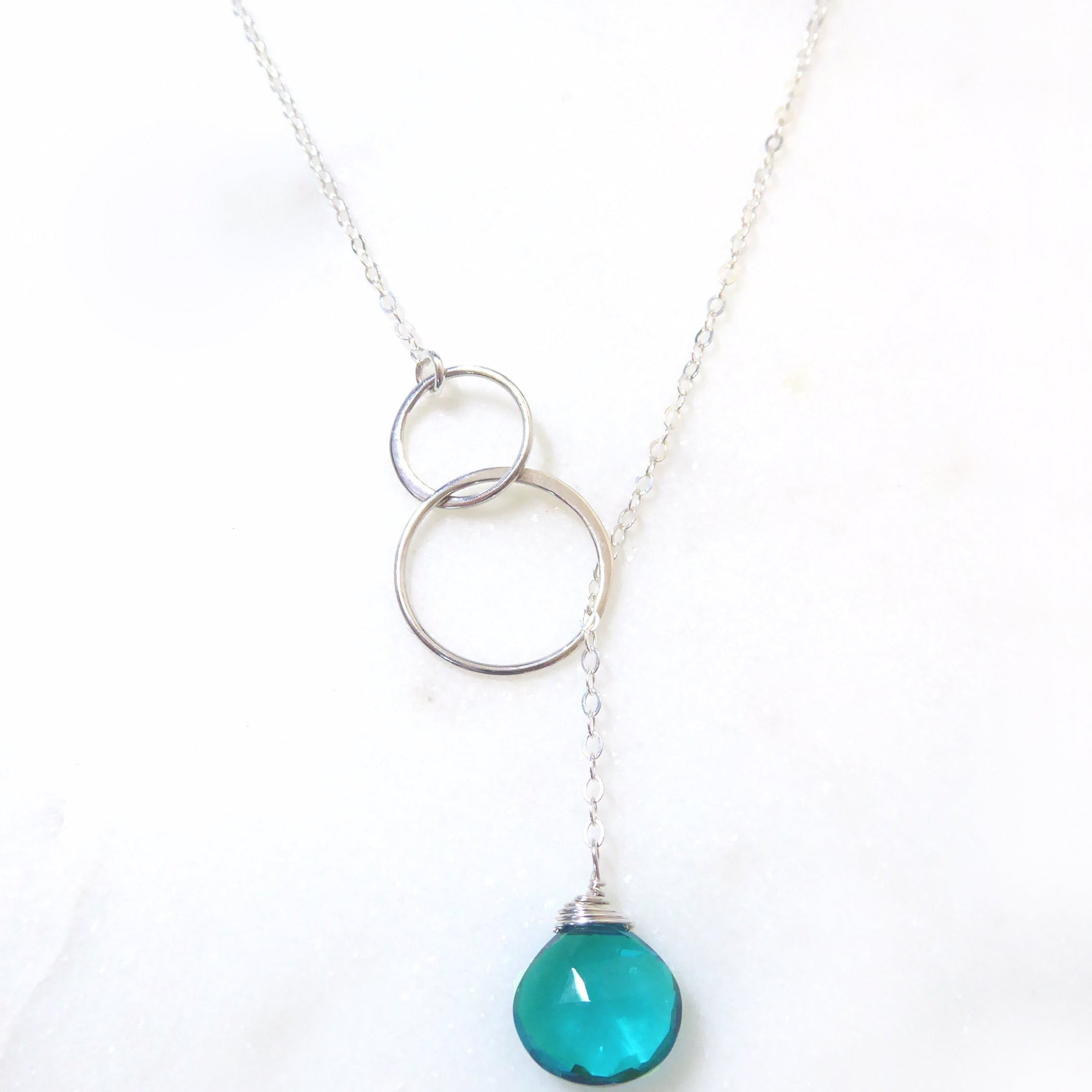 Necklace with two interlocking silver rings and a teal pendant on a white background