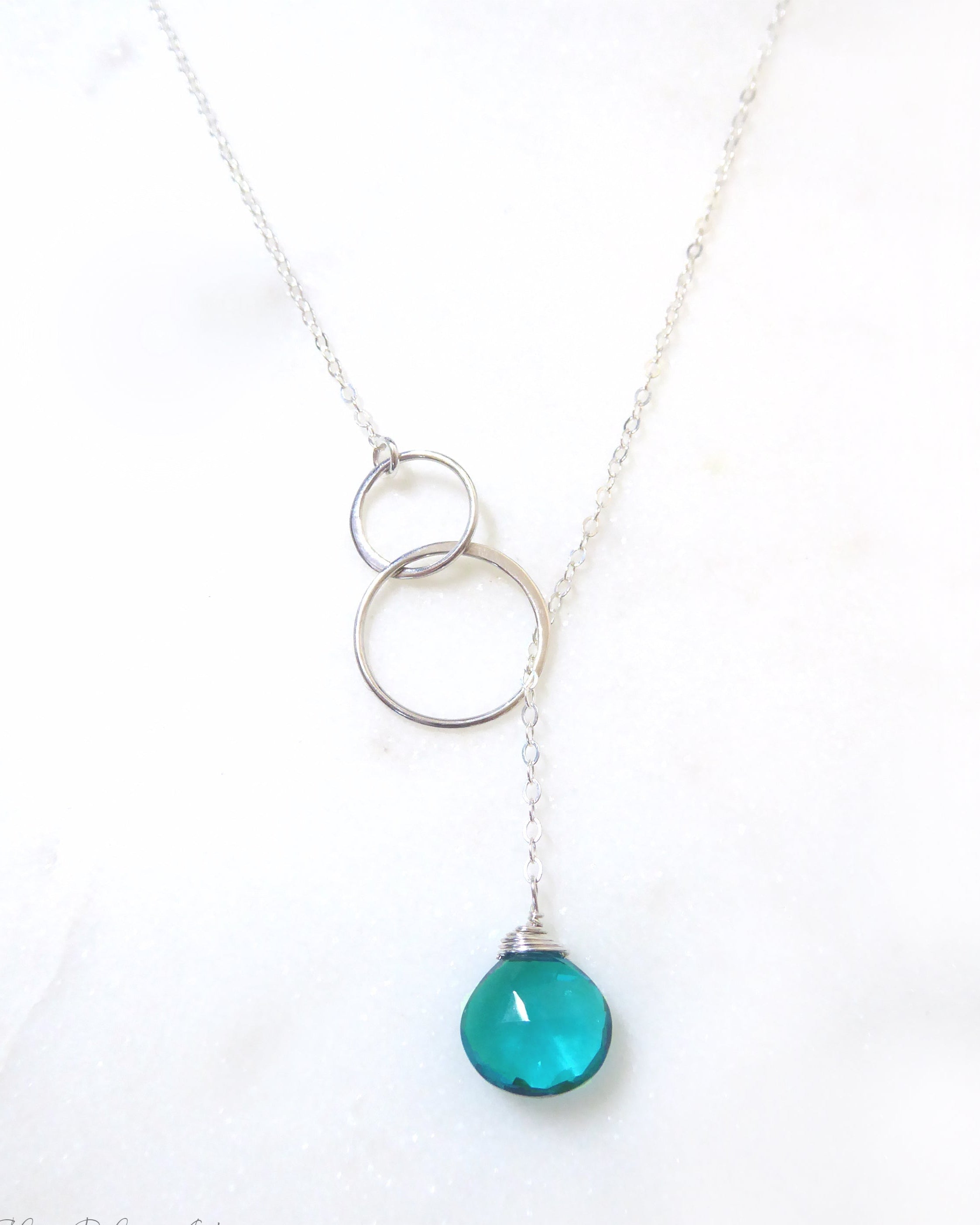 Necklace with two interlocking silver rings and a teal pendant on a white background