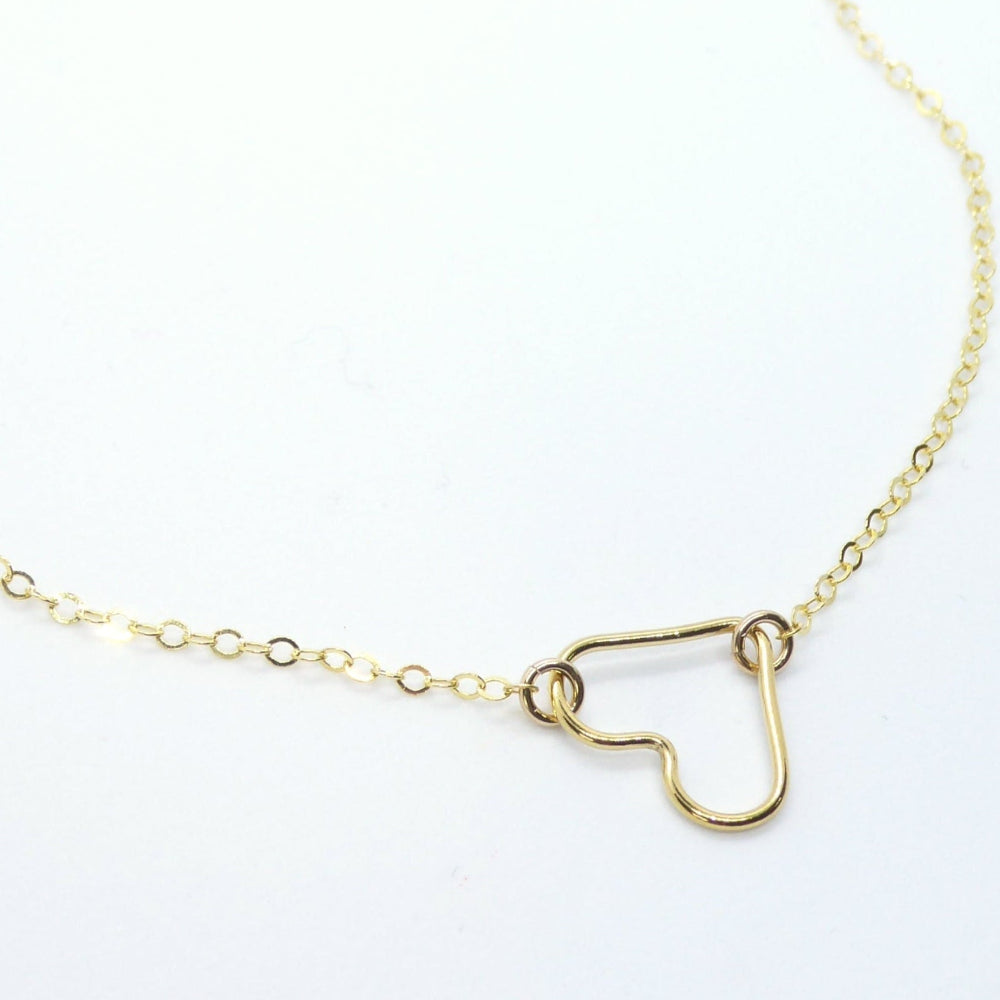A delicate gold chain necklace featuring a small, open heart-shaped pendant, photographed on a clean white background.