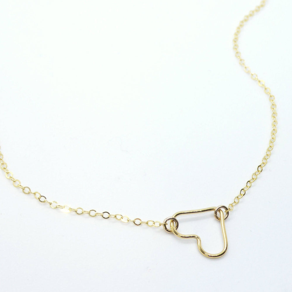 A delicate gold chain necklace featuring a small open heart pendant, displayed on a clean white background with a faint watermark in the lower-left corner.