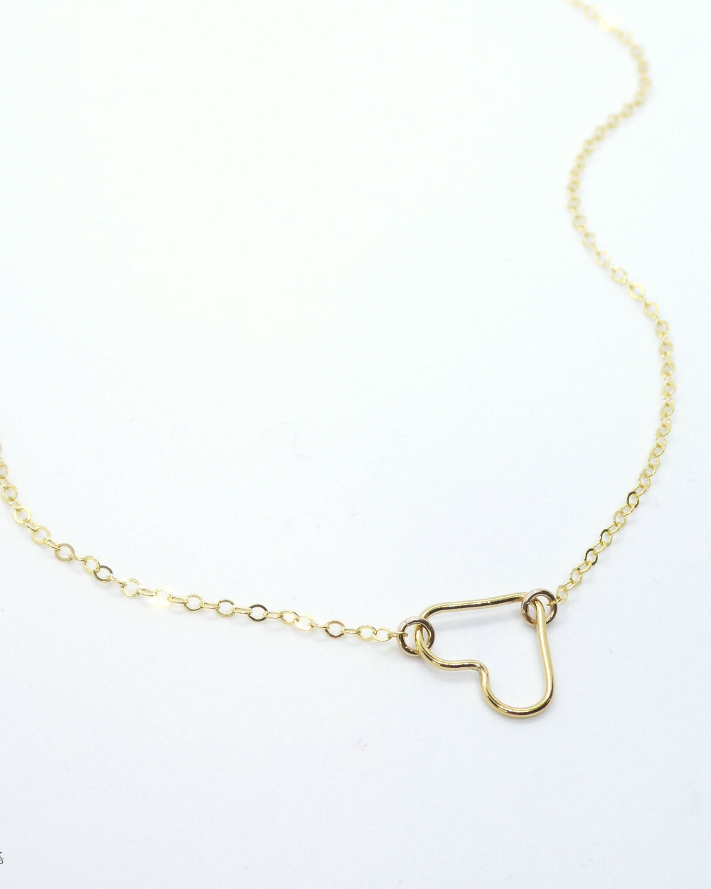 A delicate gold chain necklace featuring a small open heart pendant, displayed on a clean white background with a faint watermark in the lower-left corner.