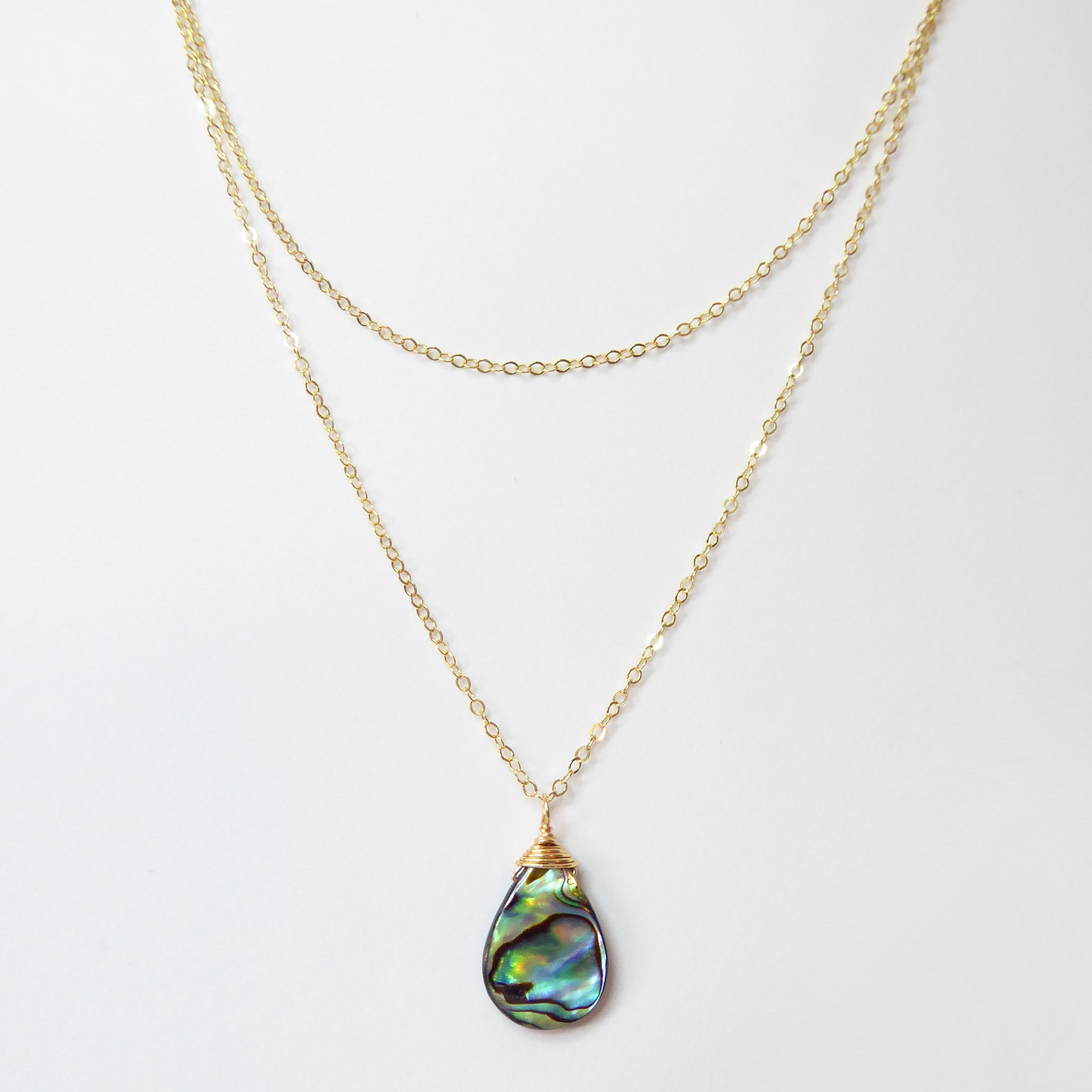 Gold necklace with a teardrop-shaped abalone shell pendant on a white background