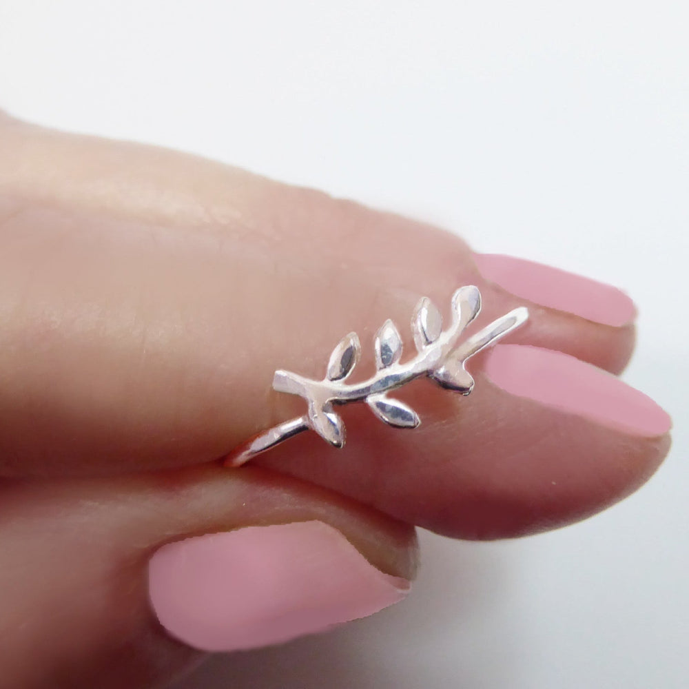 Silver leaf-shaped ring on a hand with pink nail polish against a white background