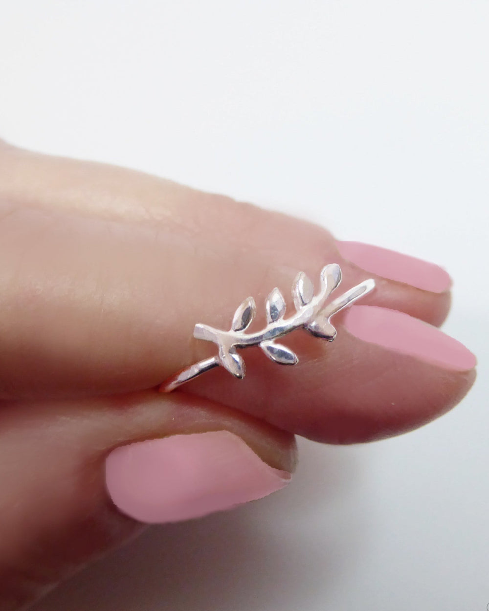 Silver leaf-shaped ring on a hand with pink nail polish against a white background