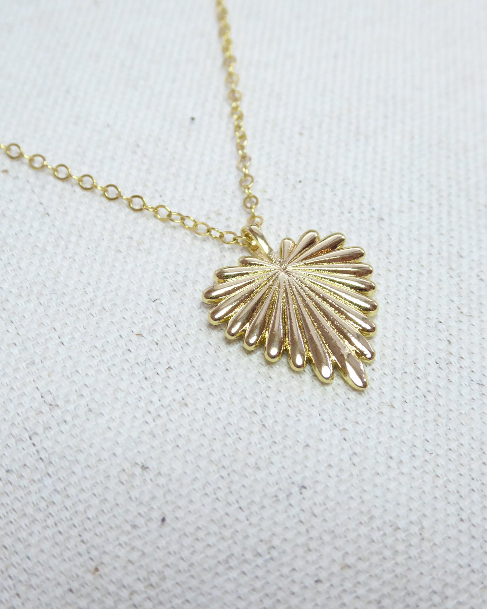 Gold shell pendant necklace on a white fabric background