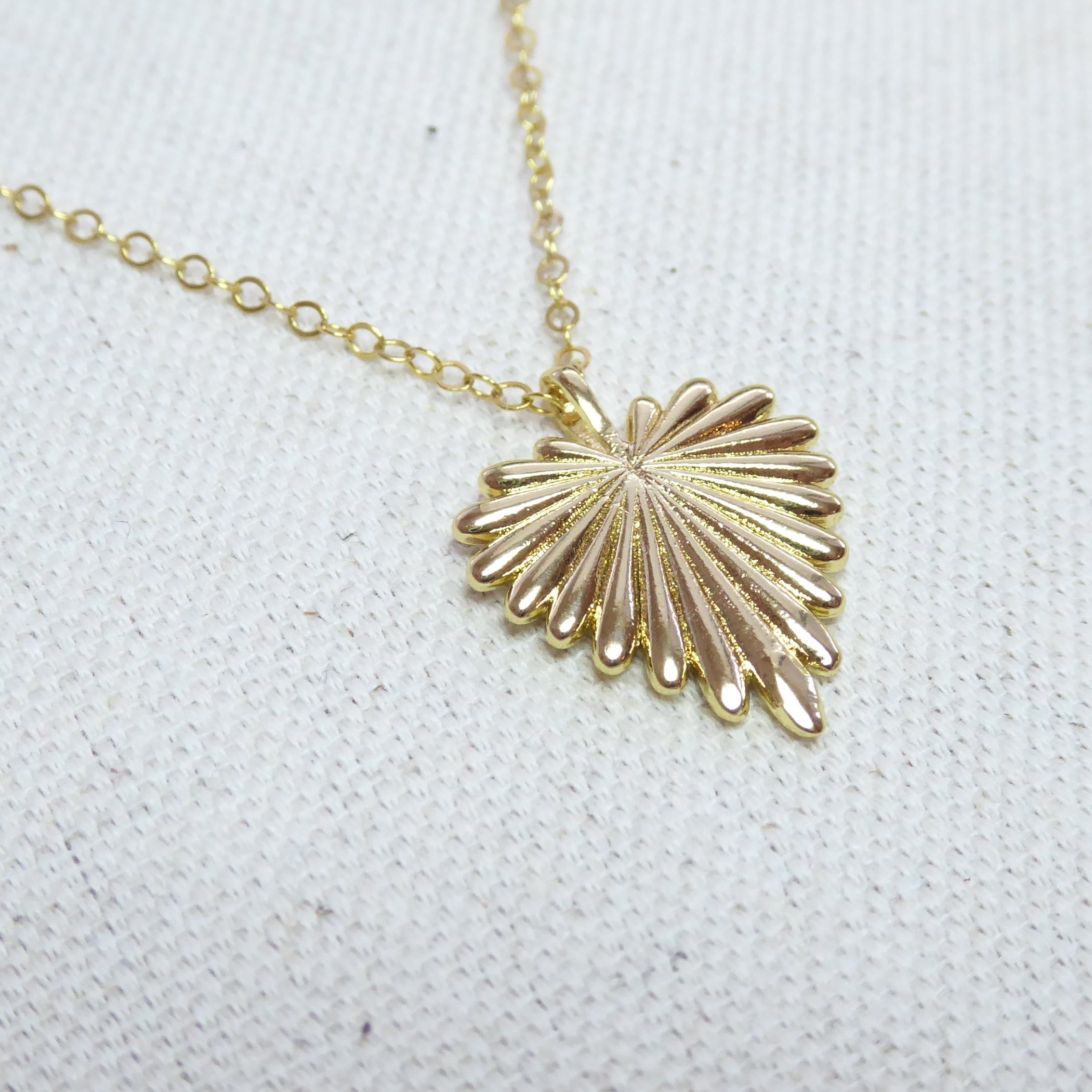 Gold necklace with a shell pendant on a white fabric background