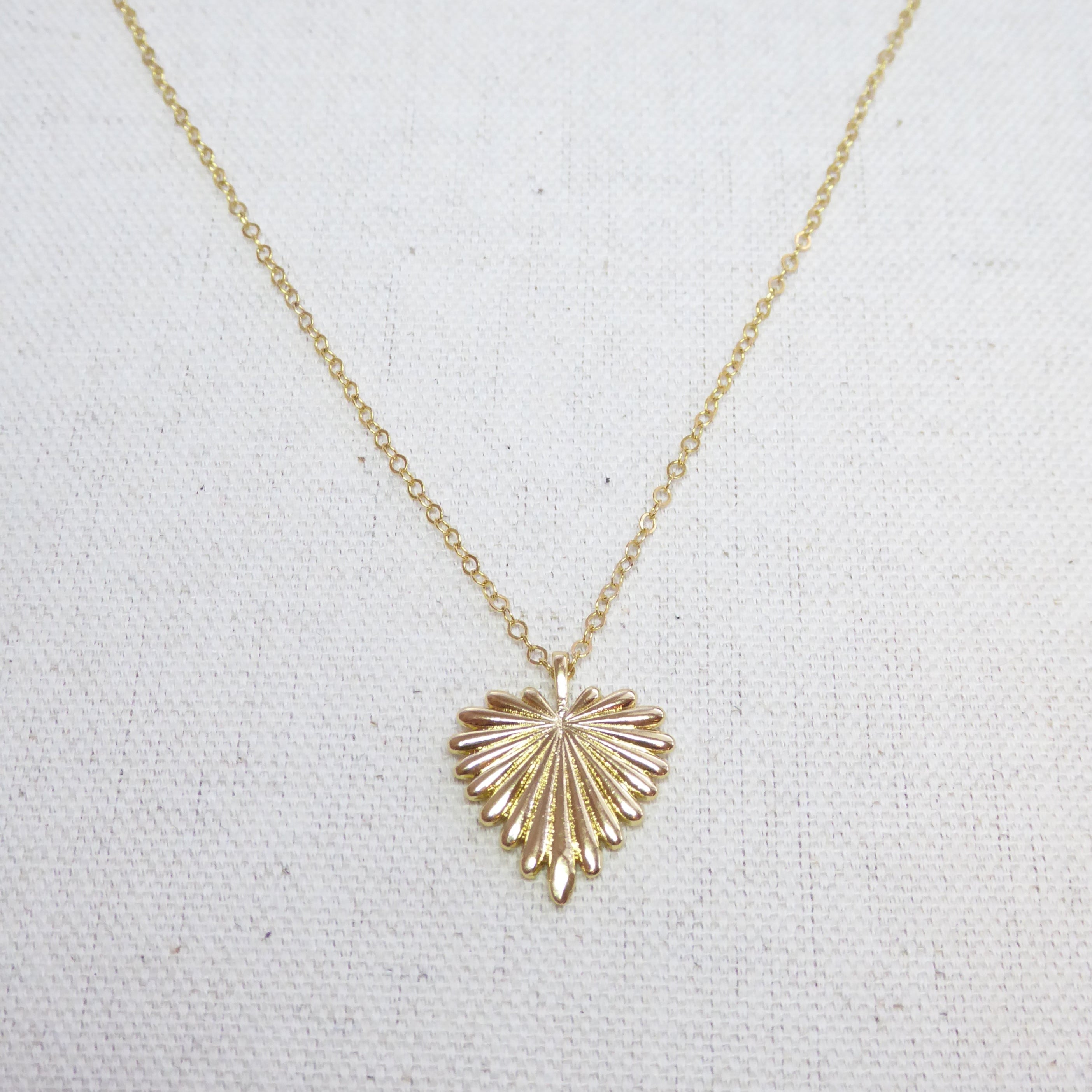 Gold necklace with a heart-shaped pendant on a light gray background