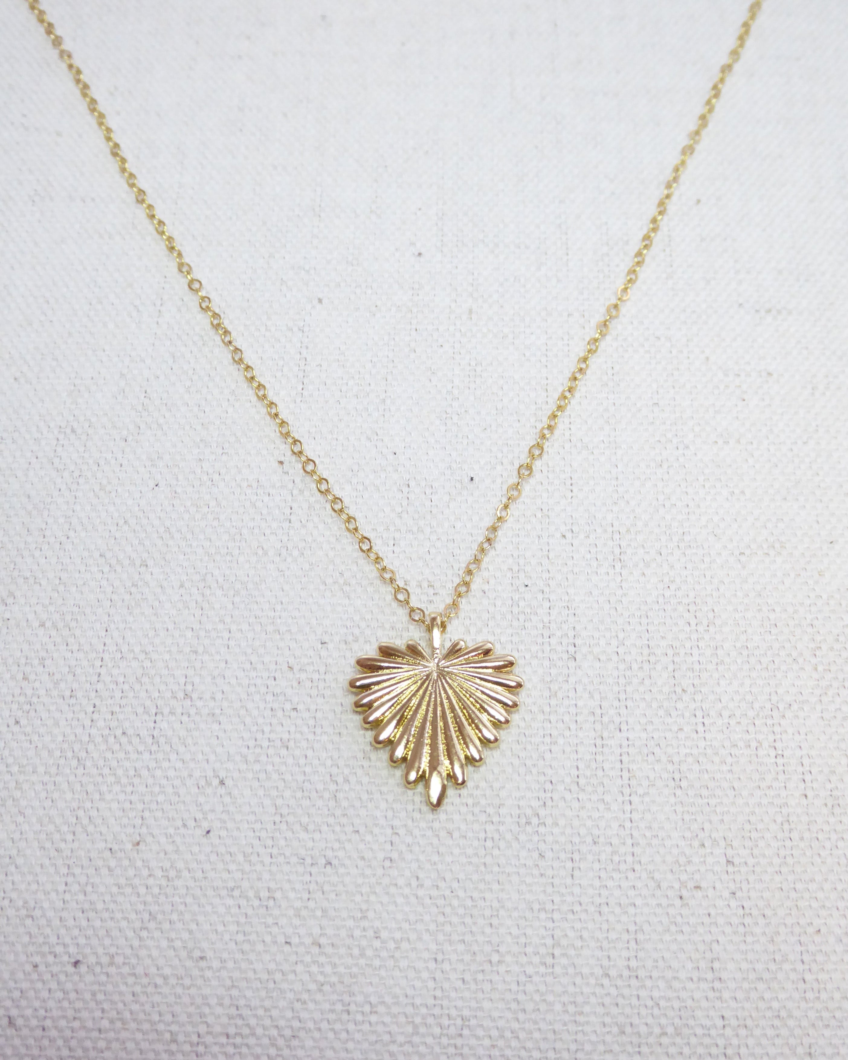 Gold necklace with a heart-shaped pendant on a light gray background