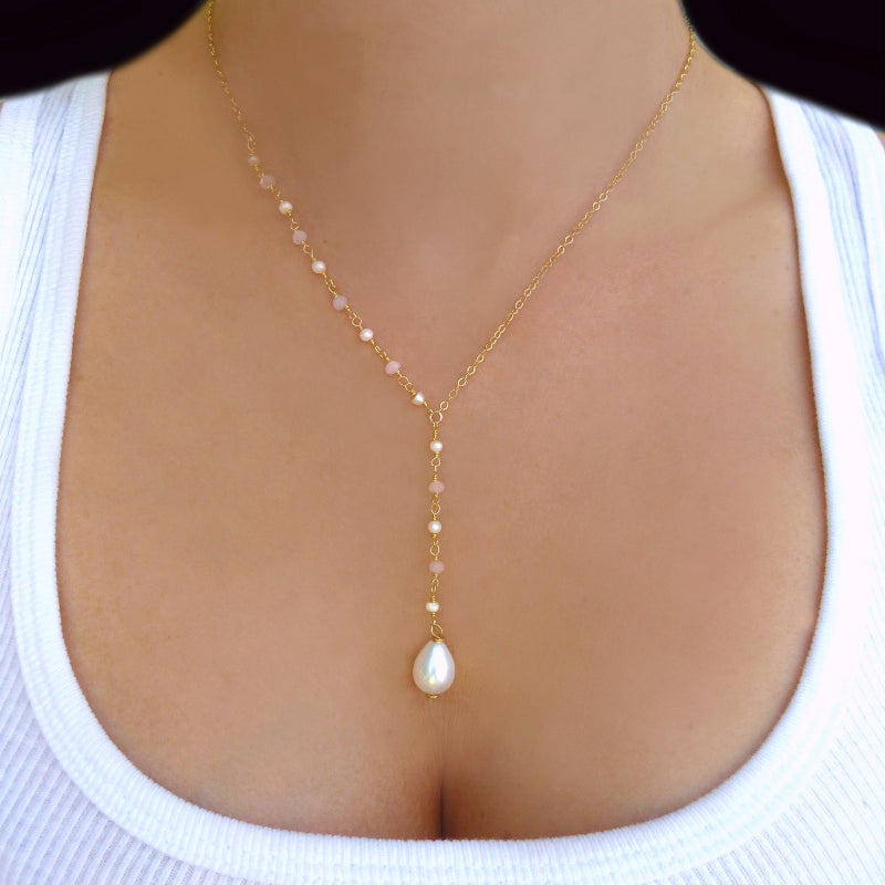 Gold necklace with a pearl pendant on a person wearing a white top.