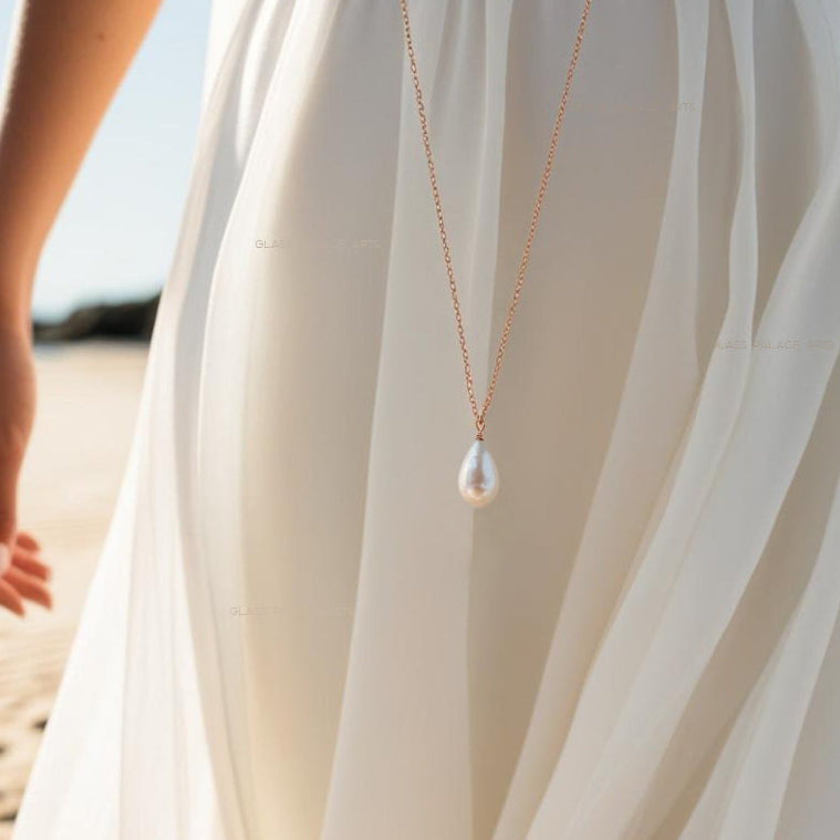 ivory pearl teardrop necklace next to woman in white dress on the beach