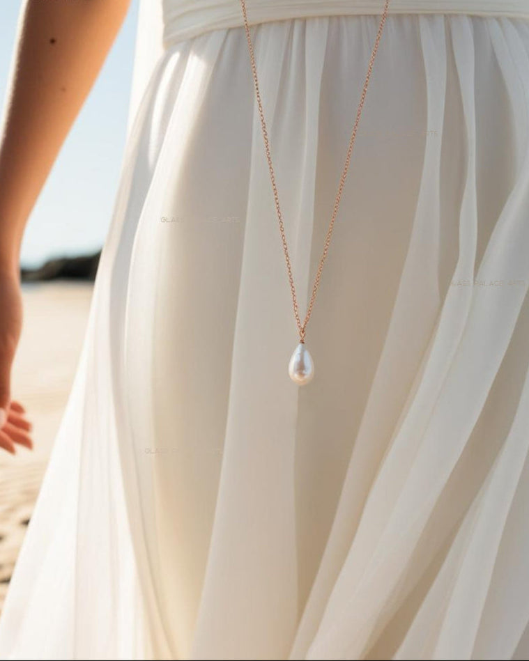 ivory pearl teardrop necklace next to woman in white dress on the beach
