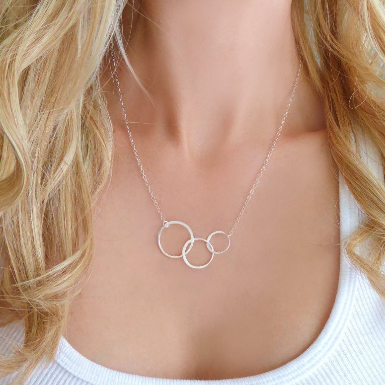 A woman wearing a three-circle infinity necklace with a shimmery chain and a gold-tone clasp.