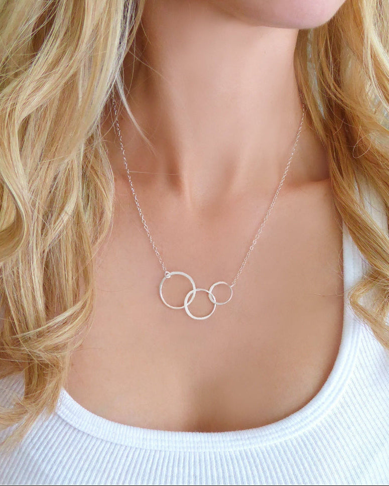 A woman wearing a three-circle infinity necklace with a shimmery chain and a gold-tone clasp.