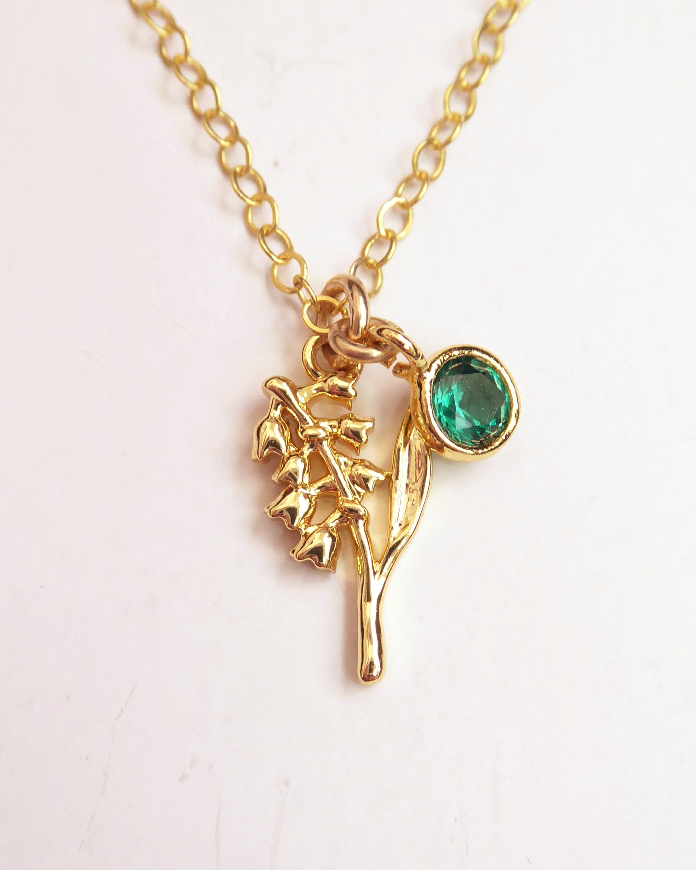 Gold necklace with a green gemstone pendant on a white background