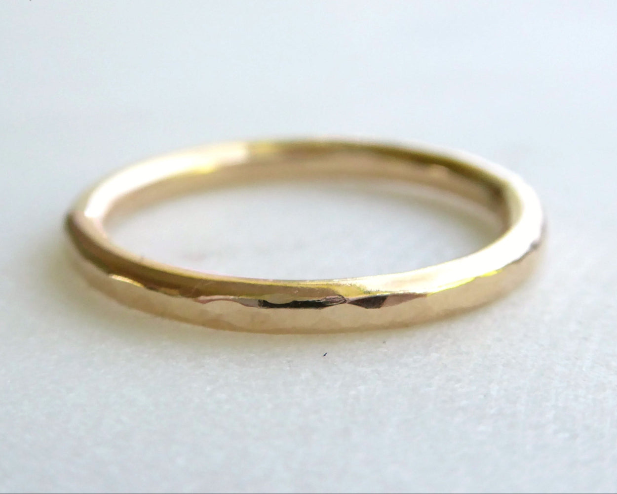 A shiny, gold-colored, hammered texture ring on a white background.
