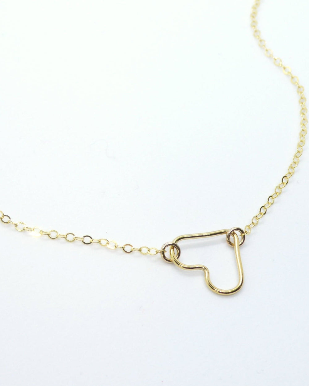 A delicate gold chain necklace featuring a small, open heart-shaped pendant, photographed on a clean white background.