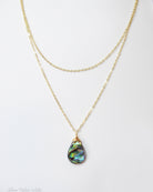 Gold necklace with a teardrop-shaped abalone shell pendant on a white background
