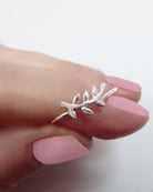 Silver leaf-shaped ring on a hand with pink nail polish against a white background