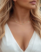 Woman wearing a white top and gold necklace with a blurred natural background