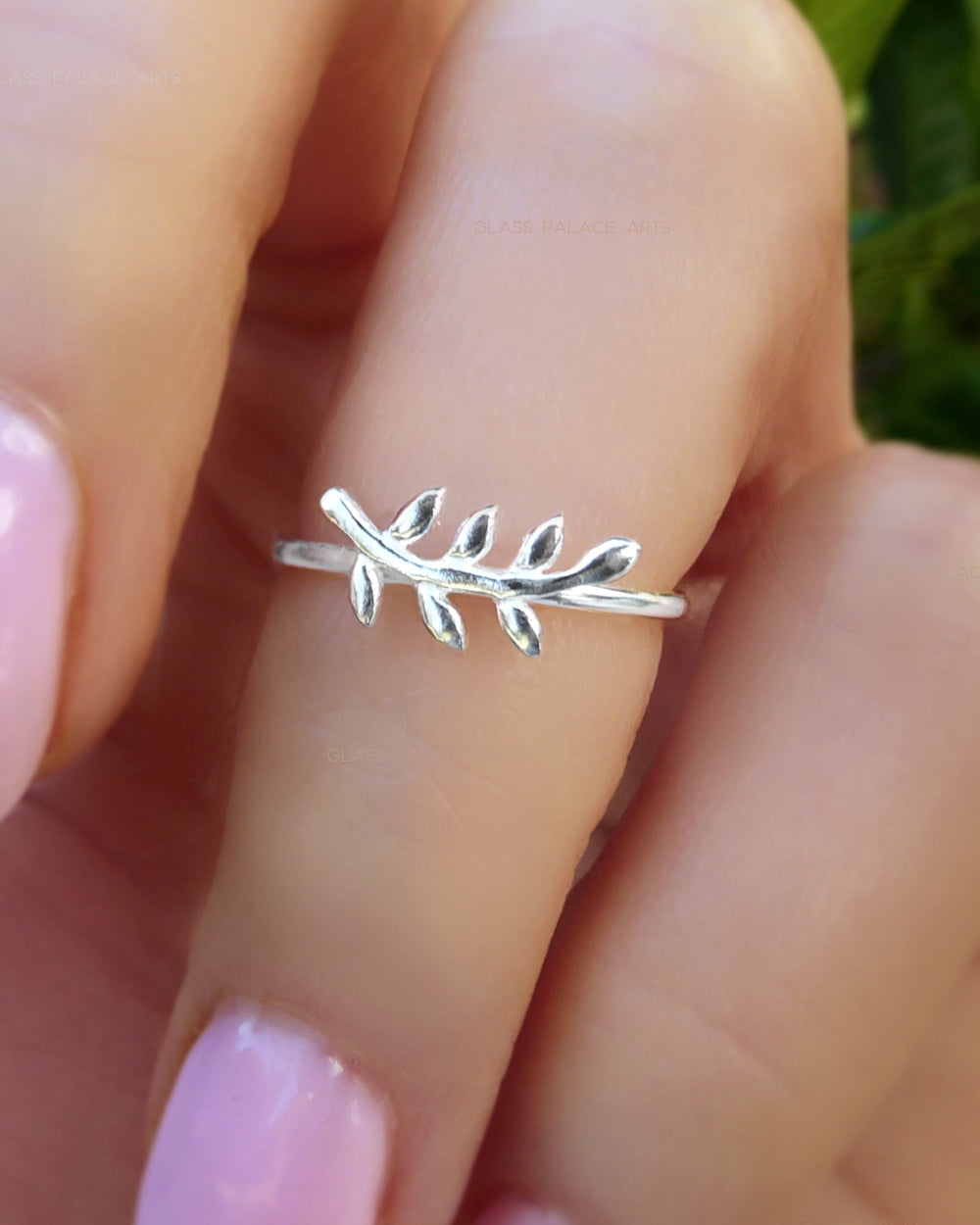 Silver leaf ring on a finger with a blurred natural background