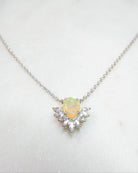 A delicate silver chain necklace featuring a central oval opal pendant surrounded by small clear stones, displayed on a light marble surface. The brand name 'Glass Palace Arts' is printed in the upper background.