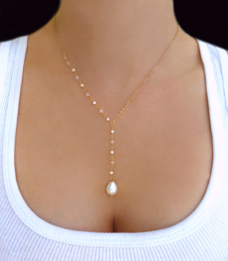 Gold necklace with a pearl pendant on a person wearing a white top.