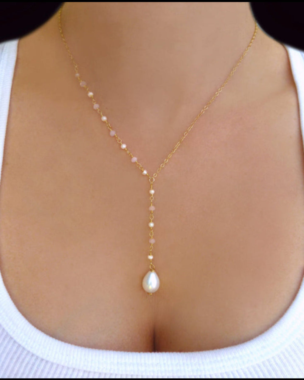 Gold necklace with a pearl pendant on a person wearing a white top.