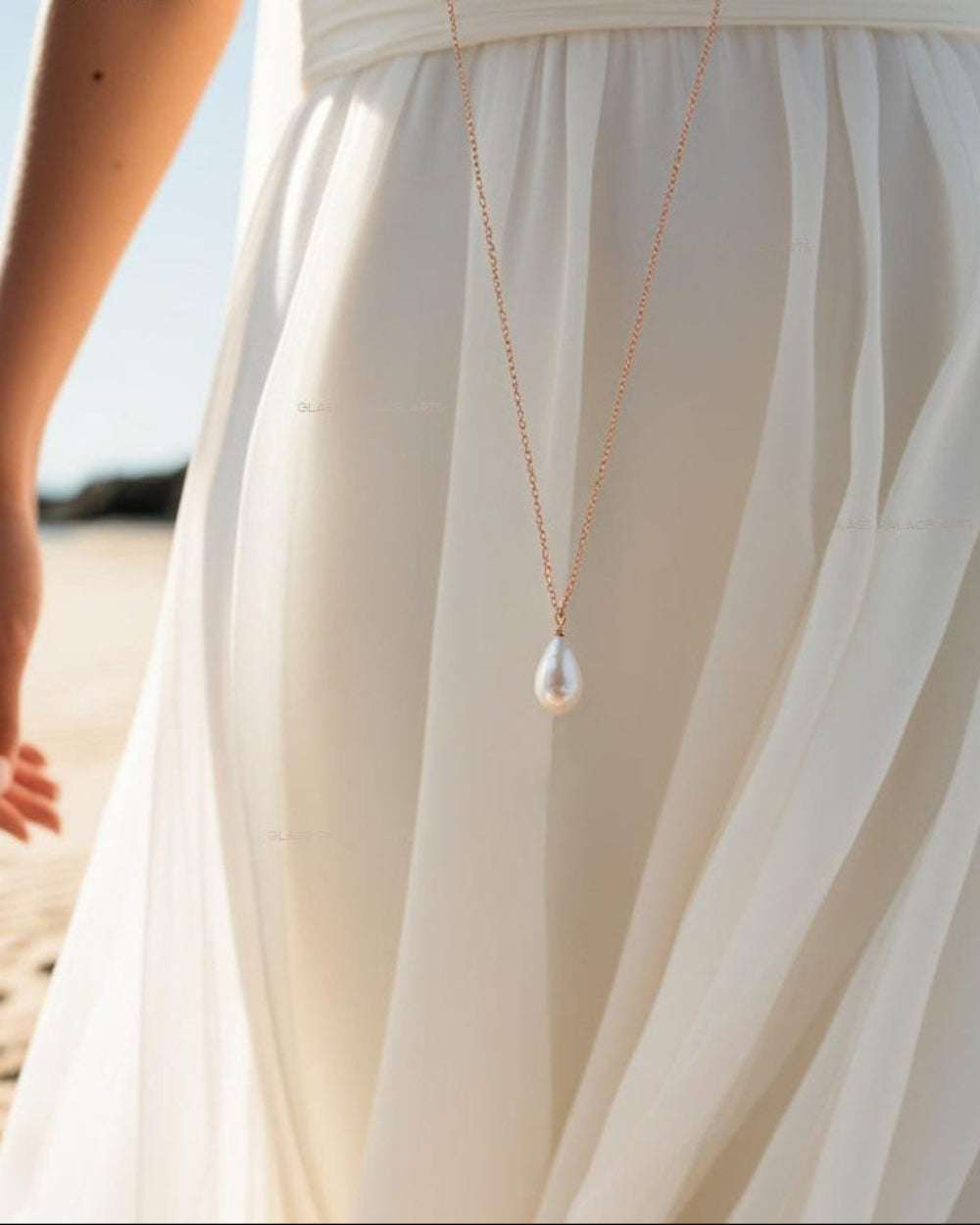 ivory pearl teardrop necklace next to woman in white dress on the beach